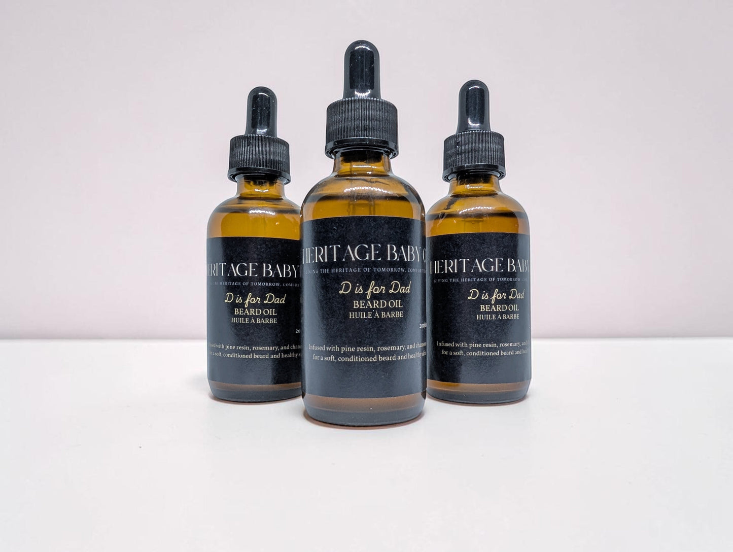 Heritage Baby Co. D is for Dad beard oil in amber glass dropper bottles with black labels, pine and rosemary scent.