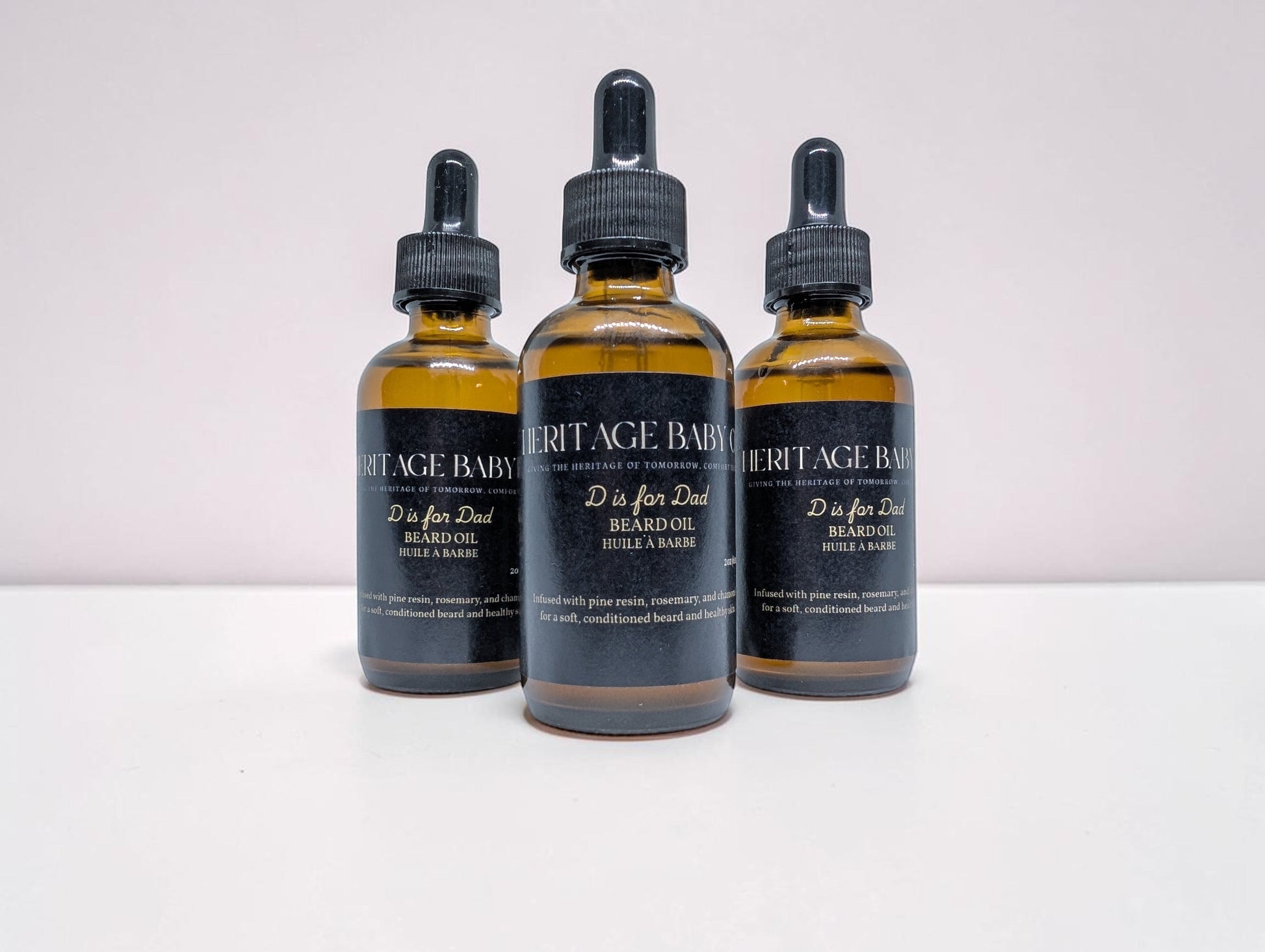 Heritage Baby Co. D is for Dad beard oil in amber glass dropper bottles with black labels, pine and rosemary scent.