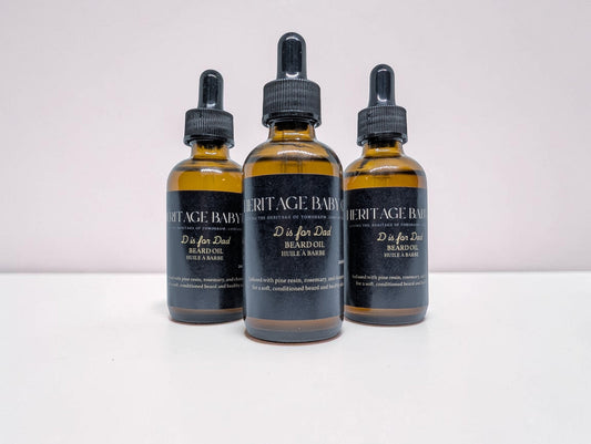 Heritage Baby Co. D is for Dad beard oil in amber glass dropper bottles with black labels, pine and rosemary scent.