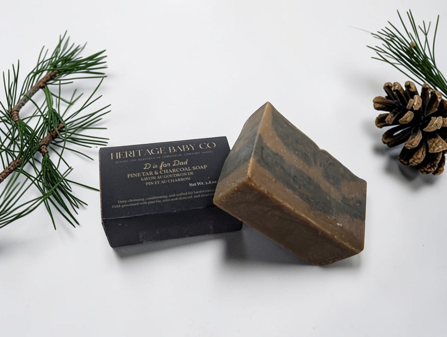 Heritage Baby Co. Pine Tar & Charcoal soap bar with a rustic, layered design next to its black product packaging.